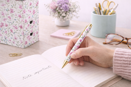 Penna a sfera con motivo floreale utilizzata per scrivere su un quaderno in un ambiente da scrivania ordinato ed elegante, ideale per l’uso quotidiano
