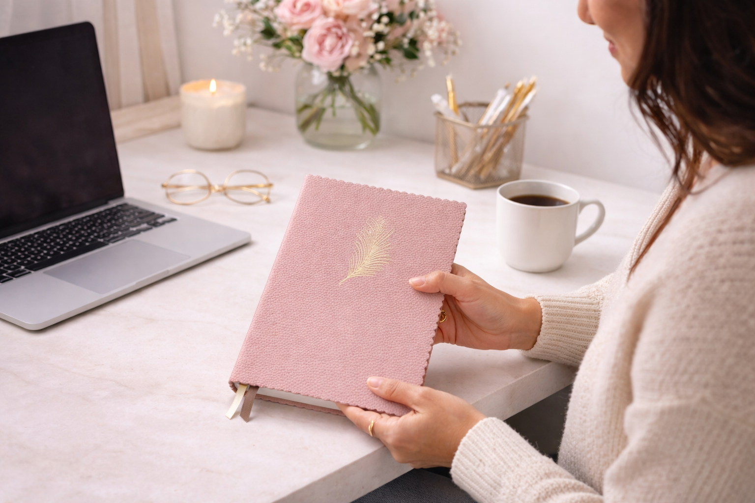 Donna seduta a una scrivania bianca e ordinata mentre utilizza un taccuino rosa elegante, in un ambiente luminoso e minimal, stile lifestyle.